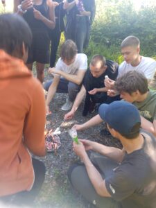 Group of teenagers toasting marshmallows around camp fire in forest